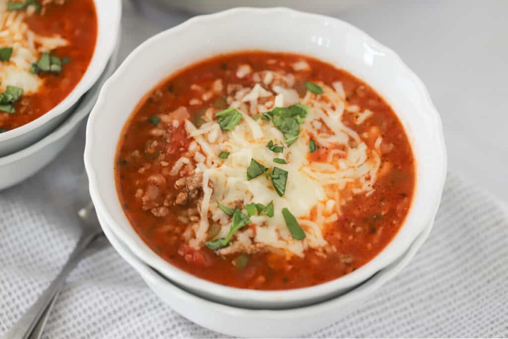 A serving bowl full of Stuffed Pepper Soup topped with melted mozzarella cheese and chopped parsley.