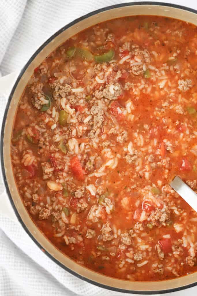 A dutch oven full of soup made with ground beef, rice, veggies and a tomato based broth.