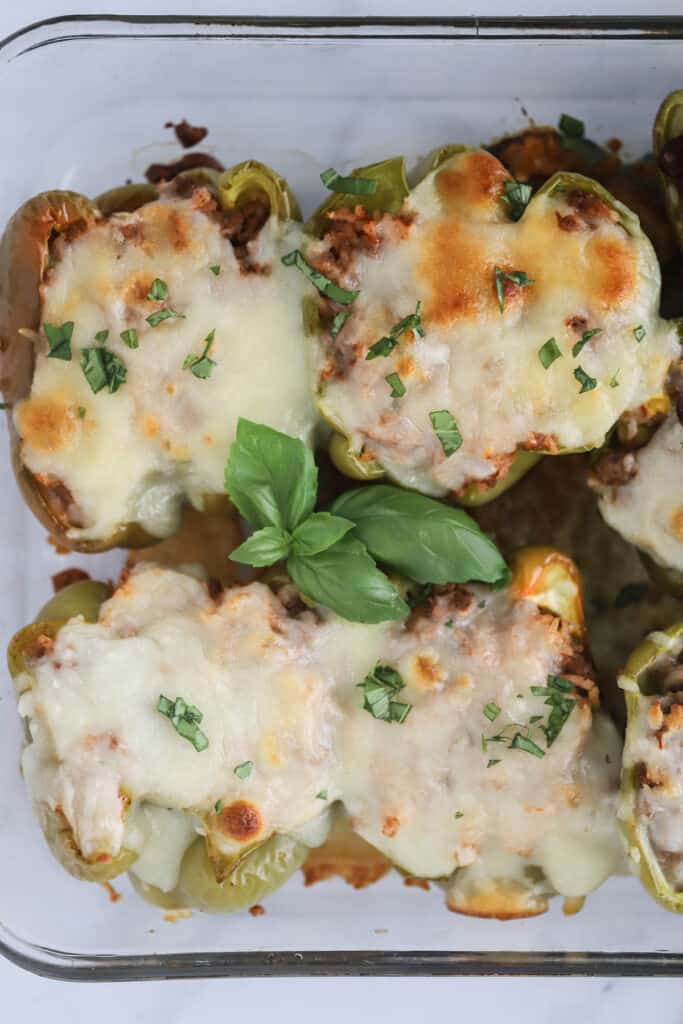 Stuffed Peppers topped with melted cheese and fresh basil in a baking dish.