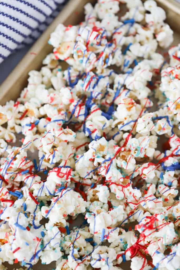 A baking tray that is covered in a layer of patriotic popcorn decorated with red, white and blue drizzle; chocolate covered popcorn recipes.