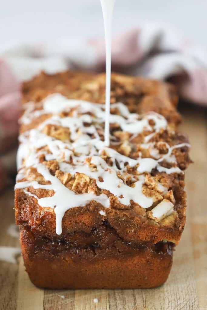 A loaf of apple cinnamon bread recipe with glaze being drizzled over the top. apple bread recipe easy.