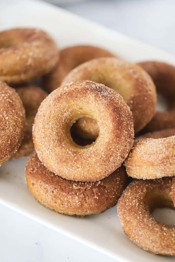 Baked apple cider donuts stacked on a large serving platter. Best baked apple cider donut recipe.