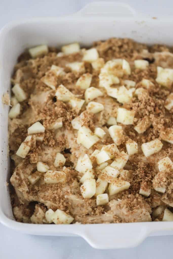 A square baking dish full of batter that's topped with apples and cinnamon sugar. cinnamon apple coffee cake.