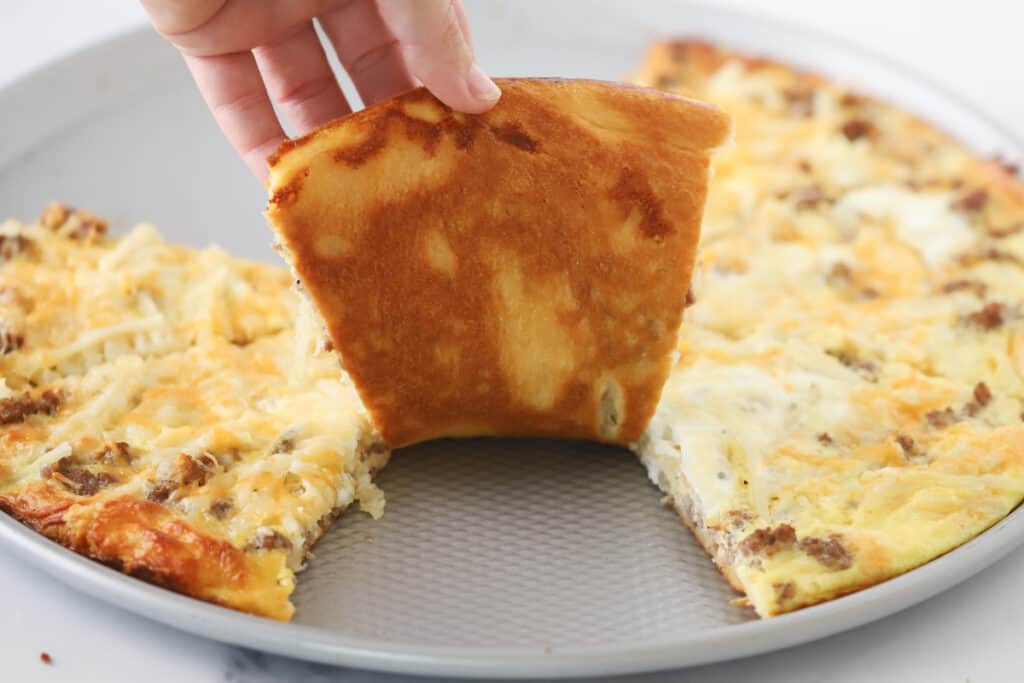A hand grabbing a slice of Breakfast Pizza from a pan. hashbrowns frozen breakfast pizza recipe. 