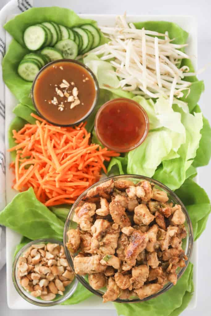 A large platter with lettuce leaves and small bowls full of sauces, chicken, and toppings to make Chicken Lettuce Wraps recipe; Best chicken lettuce wraps.