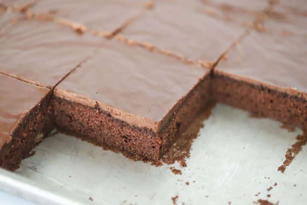A sheet pan full of Texas Chocolate Sheet Cake cut into squares with a few pieces missing.