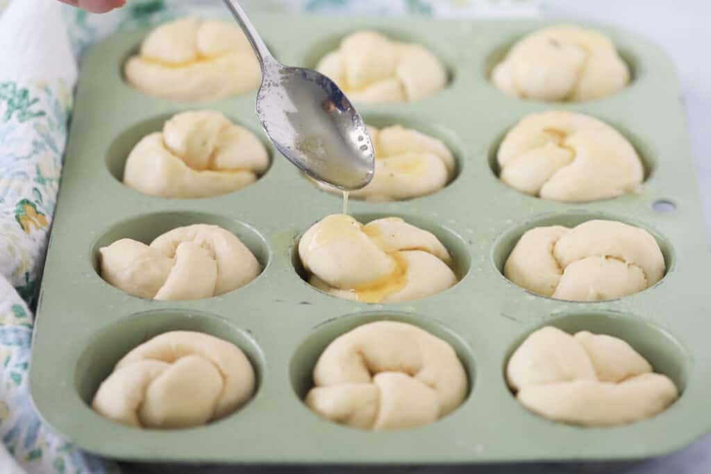 Spooning melted butter over the tops of Garlic Knots in a muffin tin. garlic knot recipe. 