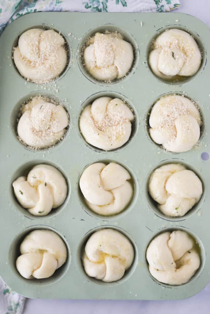 The top view of Garlic Rolls topped with Parmesan cheese inside muffin tins.