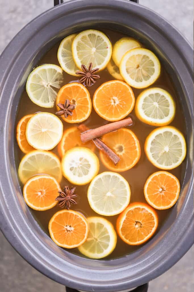 A slow cooker with Wassail ingredients including cinnamon sticks, star anise, and sliced citrus. wassail recipes. recipe for wassail, wassel, wassail recipe alcohol. 