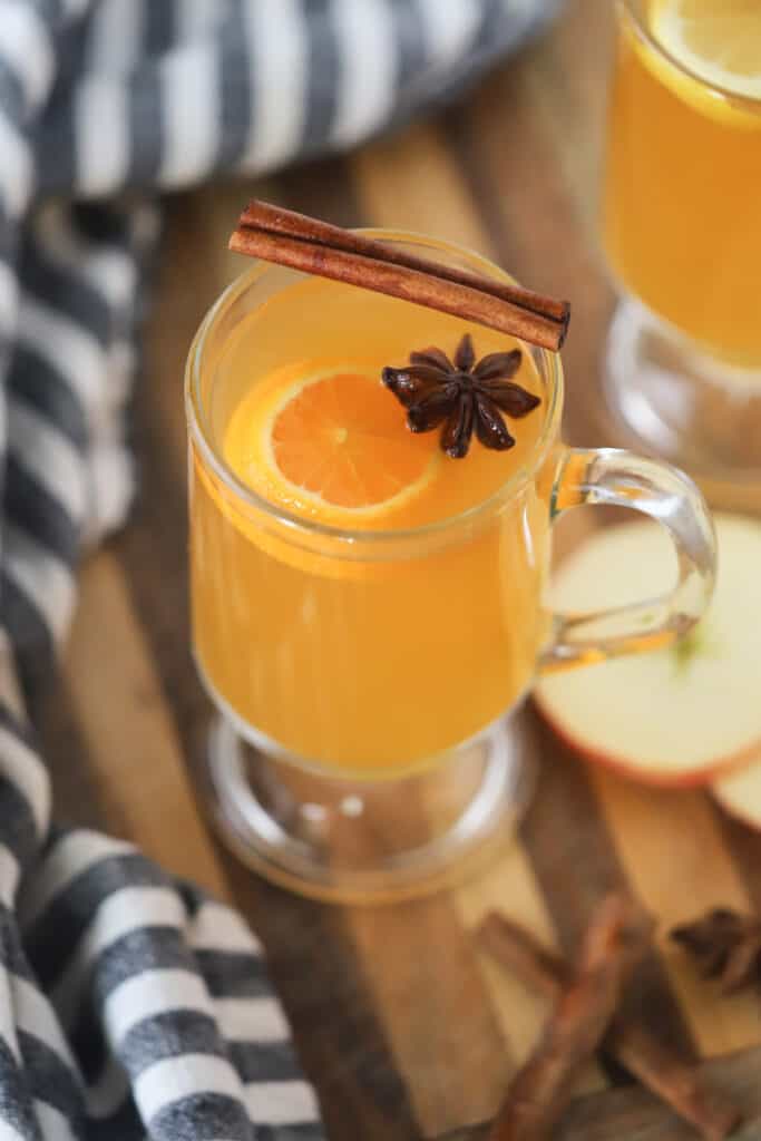 A glass mug with wassailing recipe garnished with a slice of orange, star anise, and cinnamon stick.
