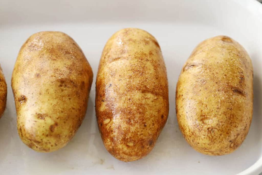 uncooked potato in a baking dish, how to make baked potato, how to bake potatoes in oven.