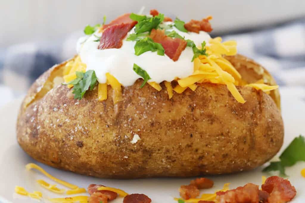 baked potato in oven with toppins, bacon, sour cream, chives, salt and pepper.