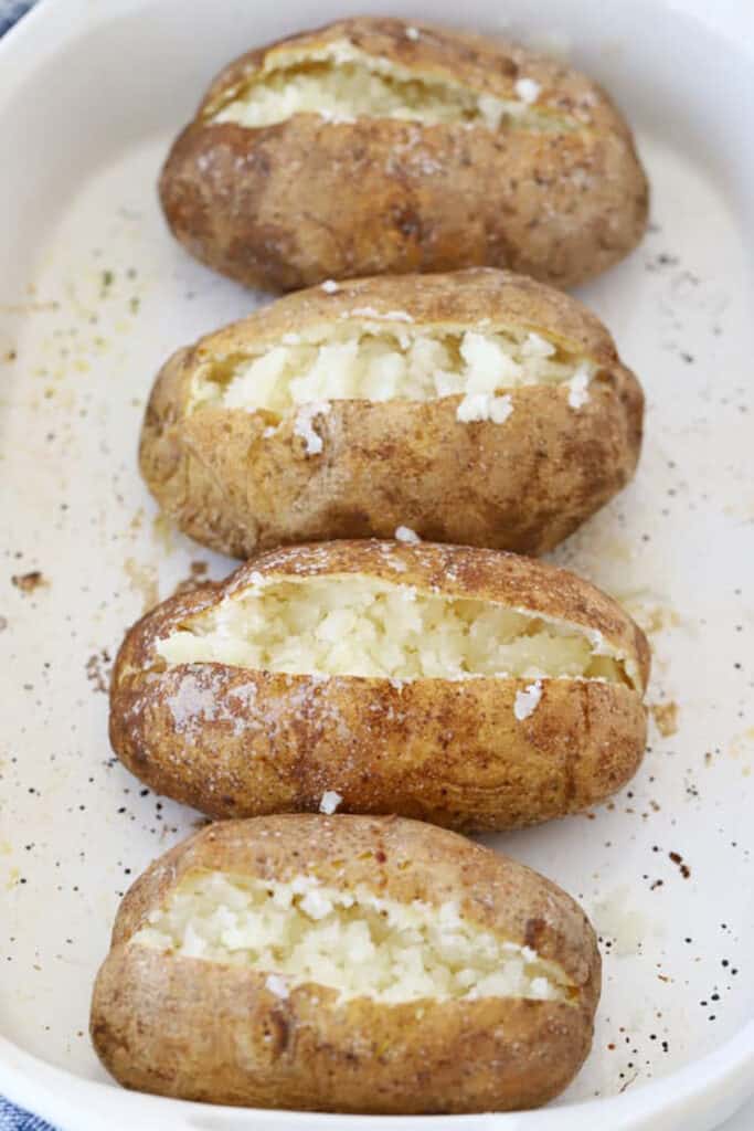 A serving dish with steakhouse baked potatoes sliced open.