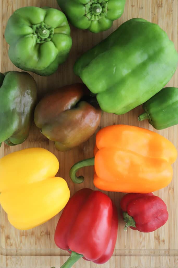 A variety of different colored bell peppers on a cutting board.