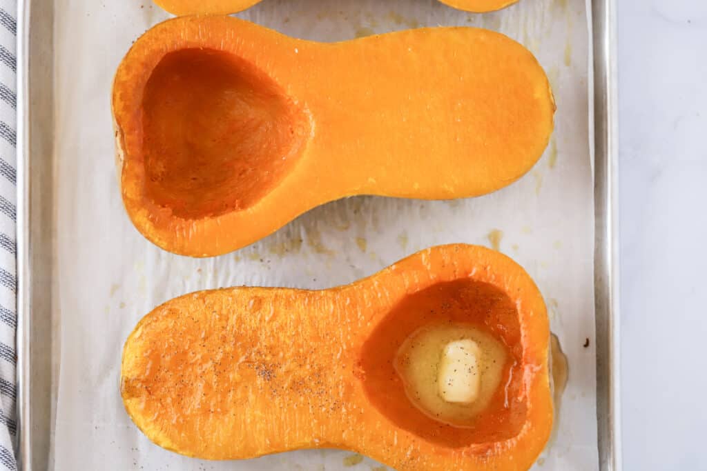 A sheet pan with roasted butternut squash halves topped with melted butter.