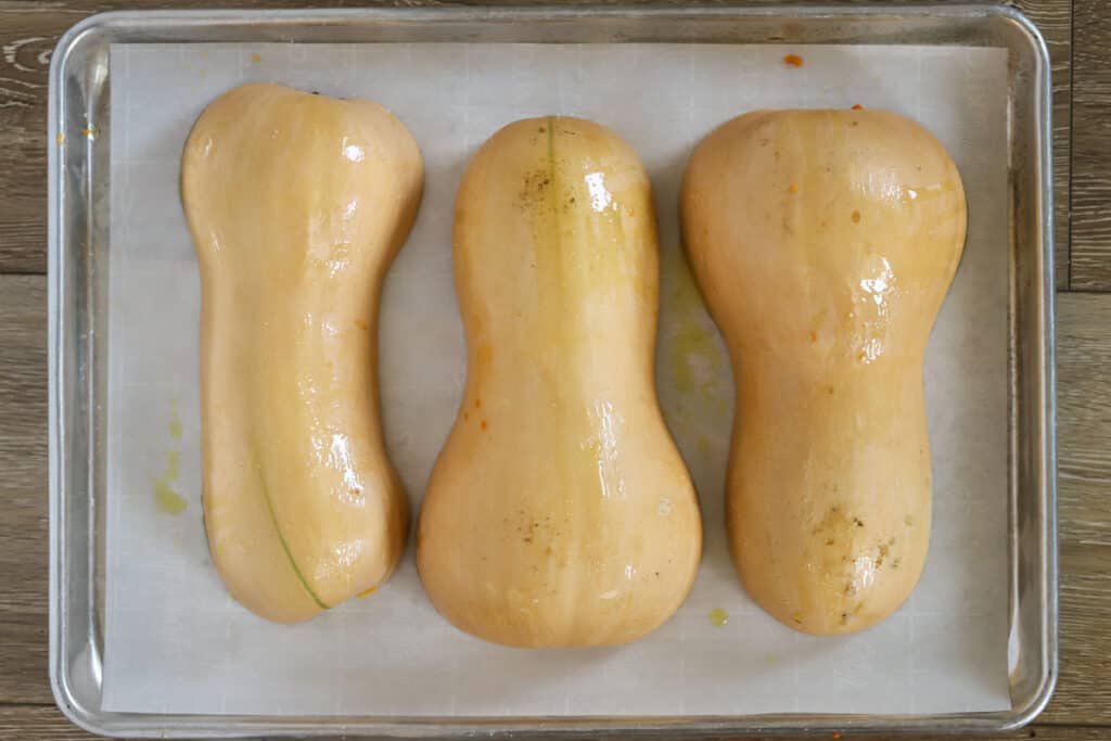 A sheet pan with three butternut squash halves, cut side down. How to roast butternut squash whole.