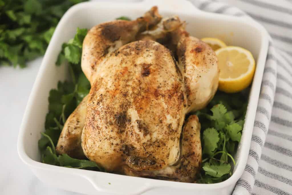 A baking dish with a whole roasted chicken surrounded by fresh parsley and lemons. rotisserie chicken crockpot recipes, rotisserie chicken tempreture. 