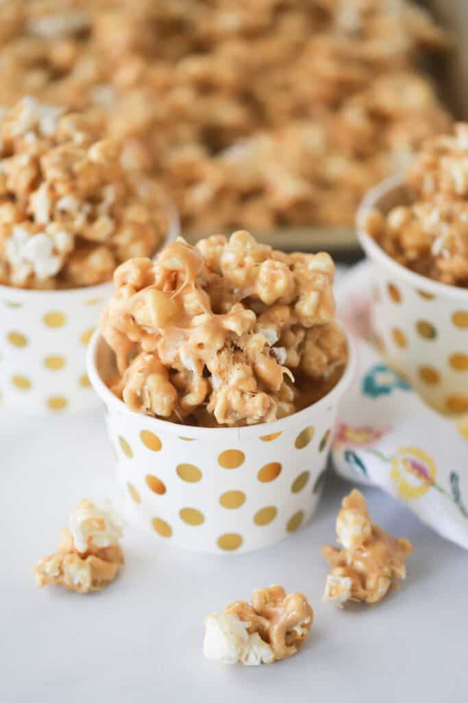 Small white cups with gold dots filled with Peanut Butter Popcorn, a simple popcorn dessert made with peanut butter, caramel, and marshmallows.