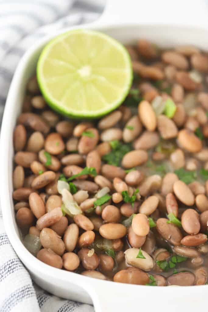 A serving dish full of cooked Pinto Beans garnished with fresh herbs and lime.
