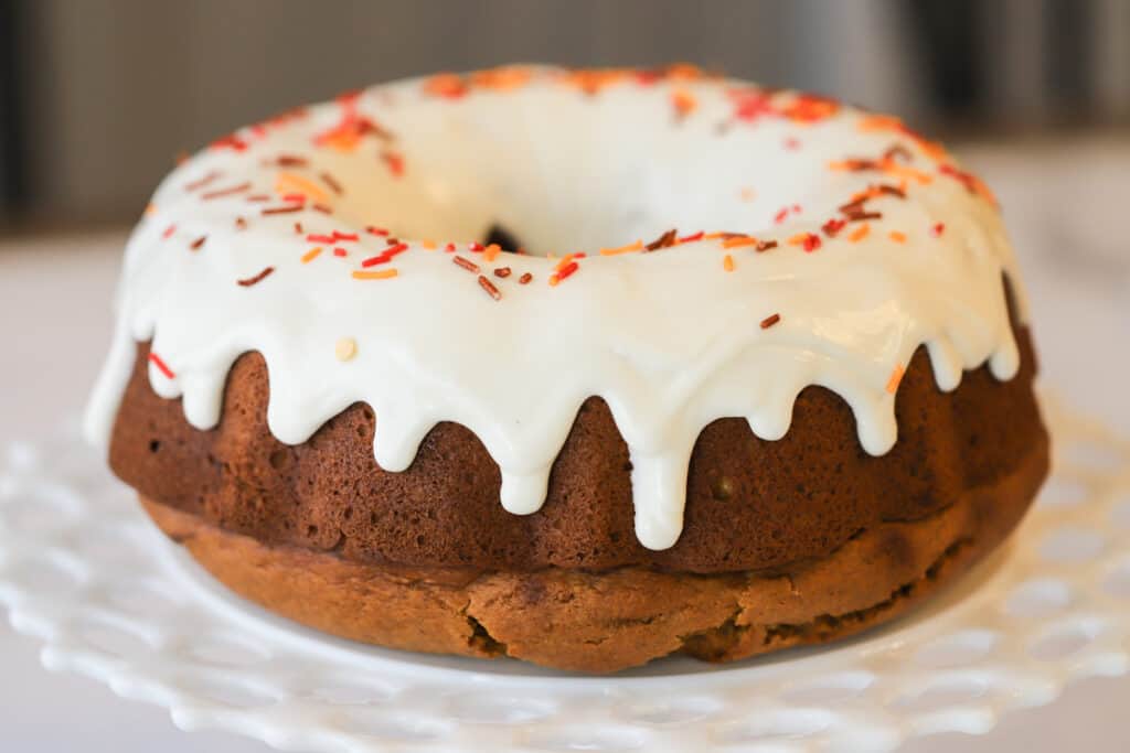 A baked bundt cake topped with glaze and sprinkles on a white serving platter.