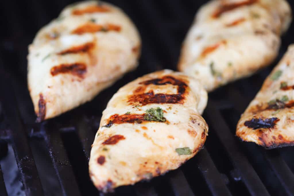Chicken breasts with grill marks cooking on a grill.
