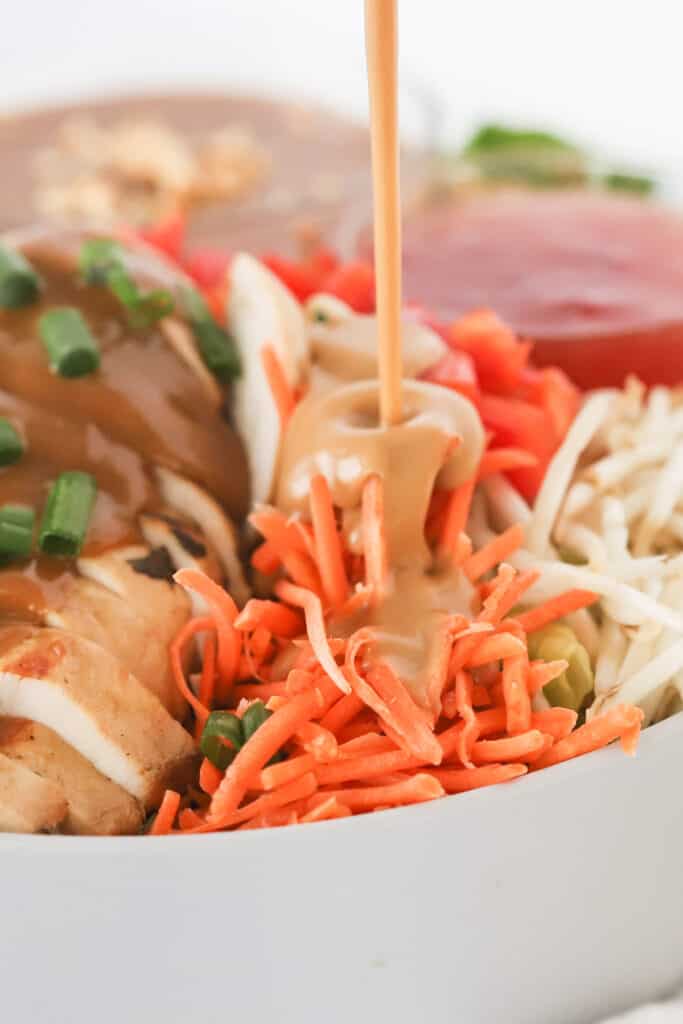 A serving bowl full of Thai Chicken Salad, with peanut dressing being poured over the top.