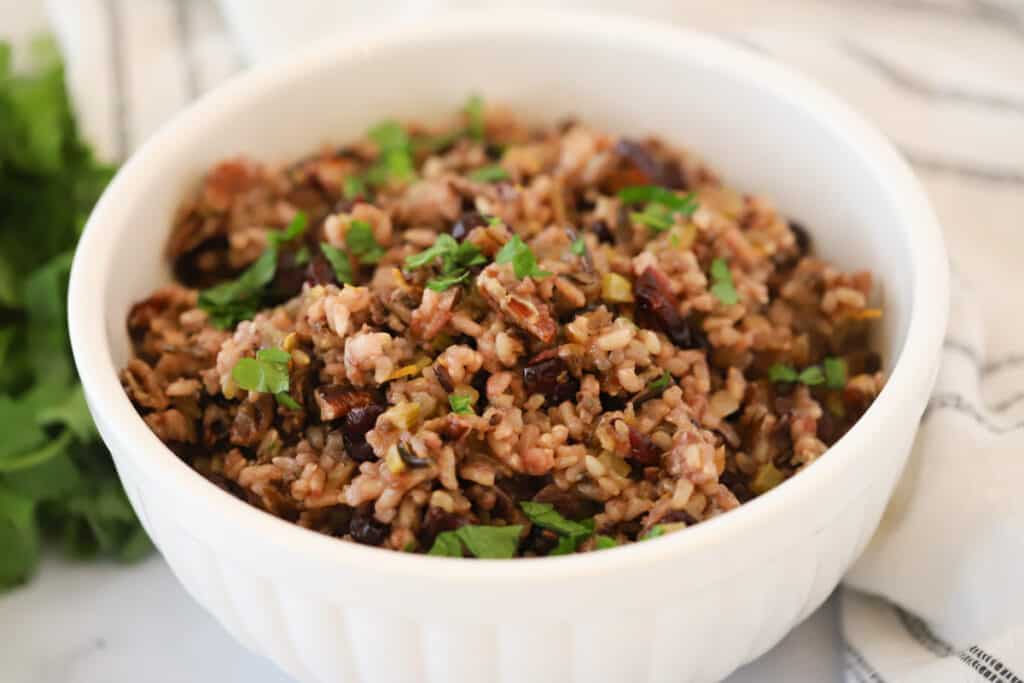 A serving bowl full of wild rice with cranberries, parsley, and pecans.