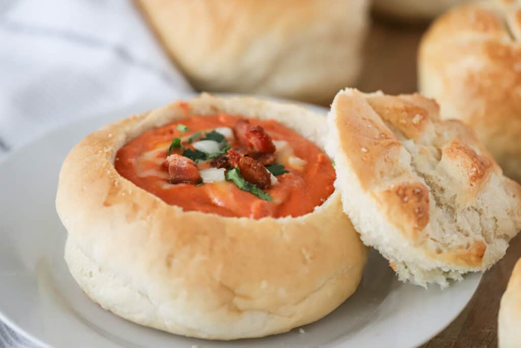 A white serving plate with a bread bowl full of soup. bread bowls recipes. How to make bread bowls, bread soup bowl, bread bowls with soup.
