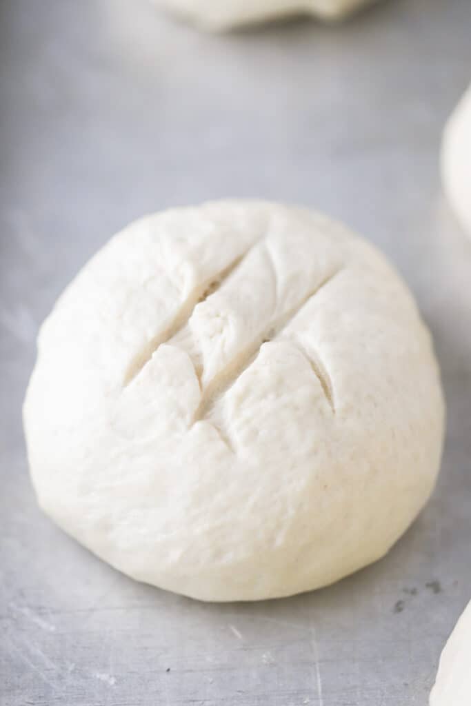 A ball of dough on a sheet tray with score marks on top. homemade bread bowls, easy bread bowl recipe, recipe for bread bowls. 