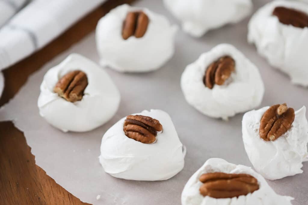Divinity candies lined up on parchment paper topped with pecans.