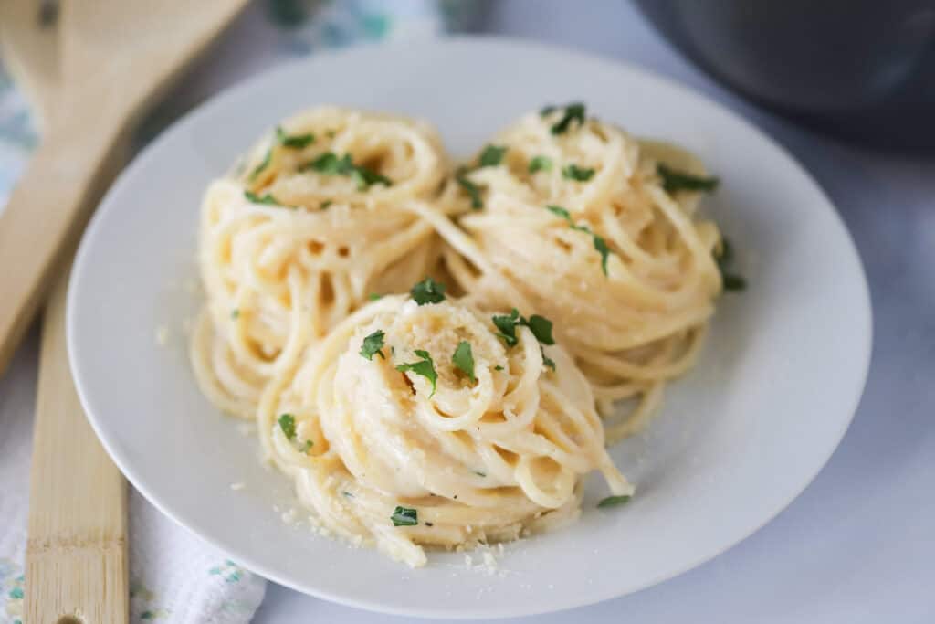 A white serving plate with spaghetti covered in creamy lemon sauce.