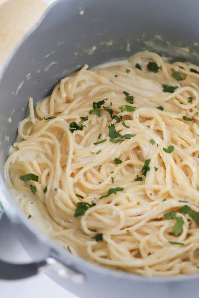 A large saucepan full of spaghetti mixed with Lemon Garlic Cream Sauce and topped with fresh parsley.