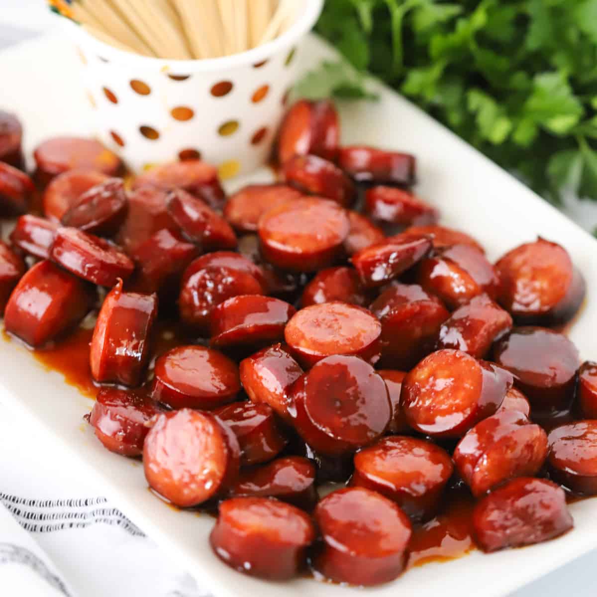 candied kielbasa on a white serving platter with fancy toothpicks