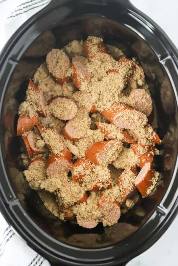 A slow cooker with sliced kielbasa covered with brown sugar.