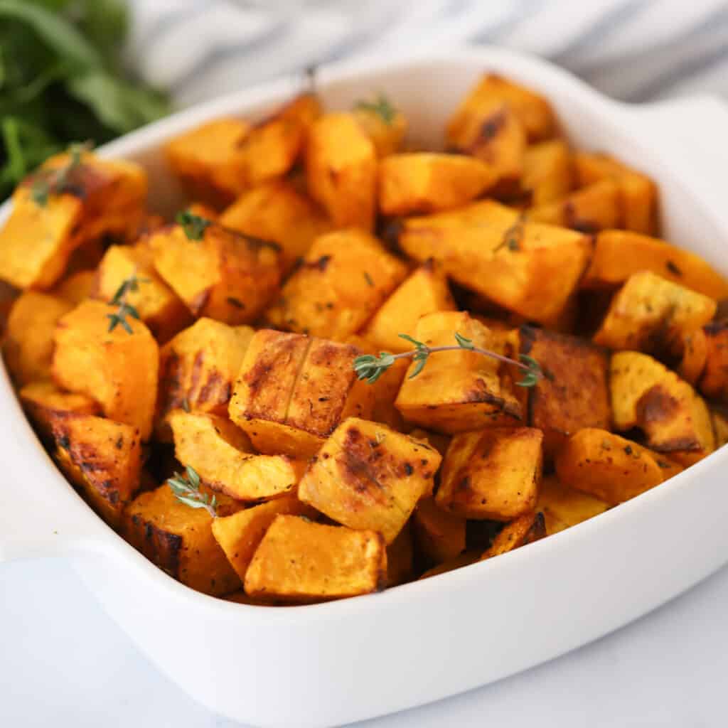 A large white serving dish full of squash roasted in oven, topped with fresh herbs.