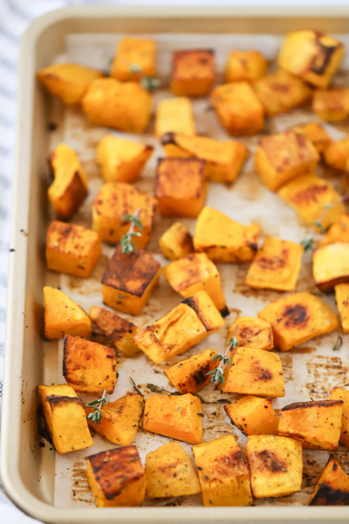 A sheet pan lined with parchment paper and covered with roasted squash cubes. How long to roast squash. Roasted squash oven recipe.