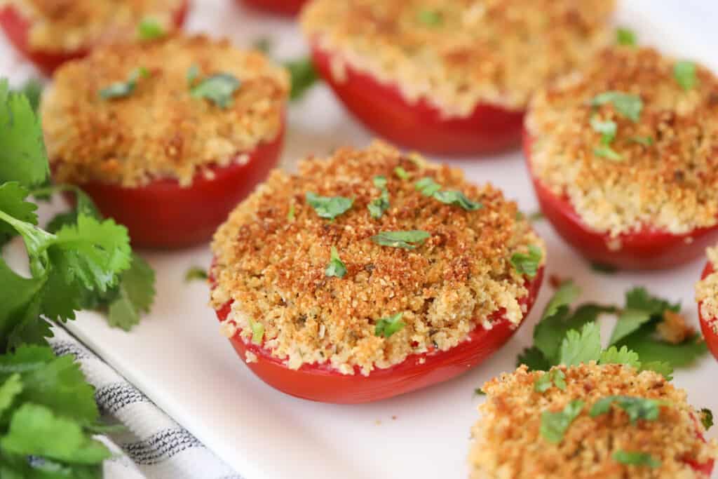 A serving platter full of baked Parmesan tomatoes topped with fresh herbs. baked tomato parmesan, baked tomato parmesan recipe. 