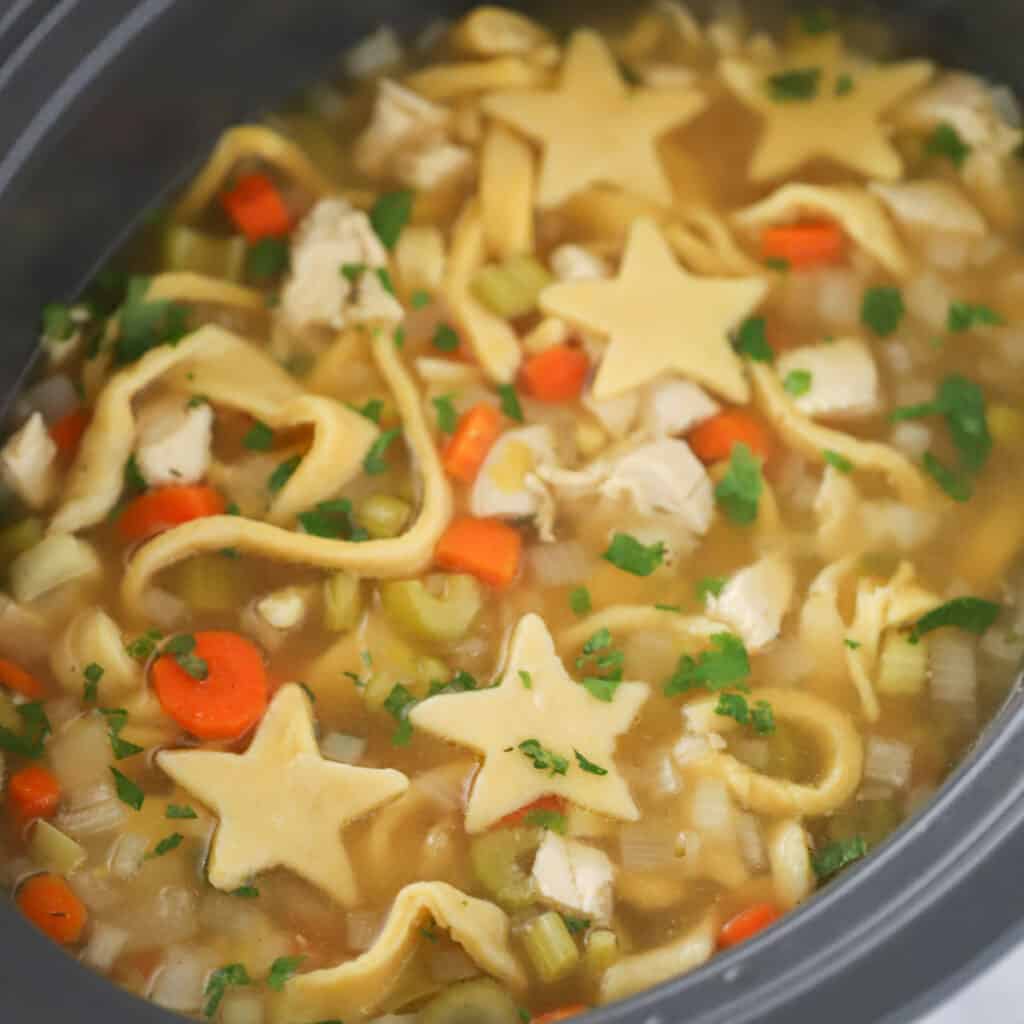 A crockpot full of chicken noodle soup with fresh egg noodles cut into star shapes. how long to cook egg noodles, what to make with egg noodles, homemade egg noodle recipe. 