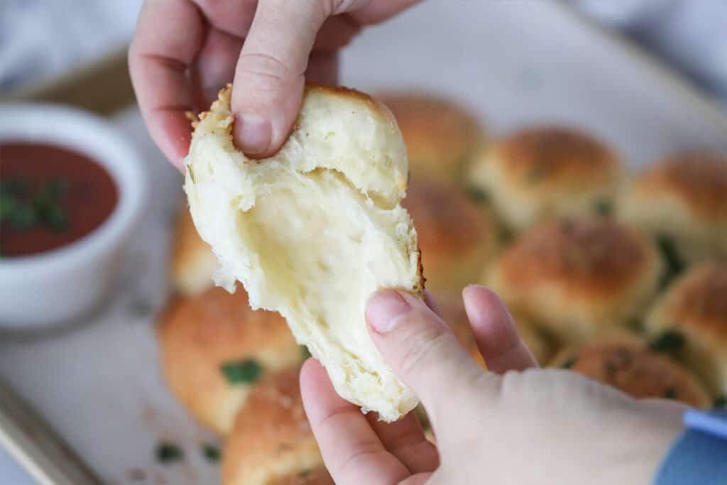 Two hands pulling apart a pull-apart roll to see melted cheese on the inside. pull apart rolls, garlic rolls recipe. 