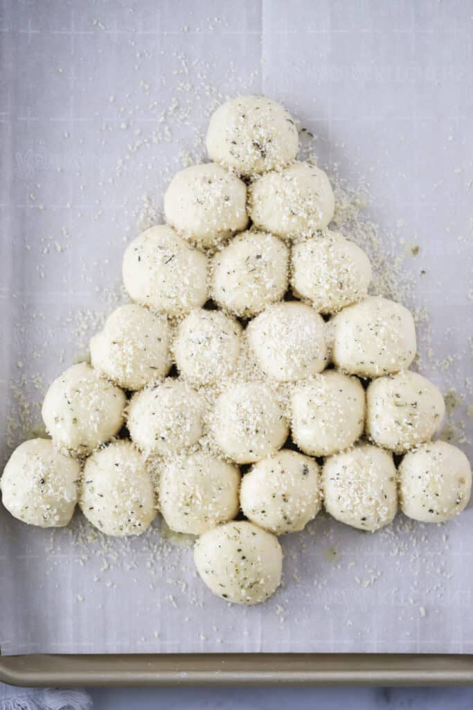 Balls of dough arranged in the shape of a Christmas tree on a baking sheet, topped with grated Parmesan cheese. garlic_roll, Christmas rolls.