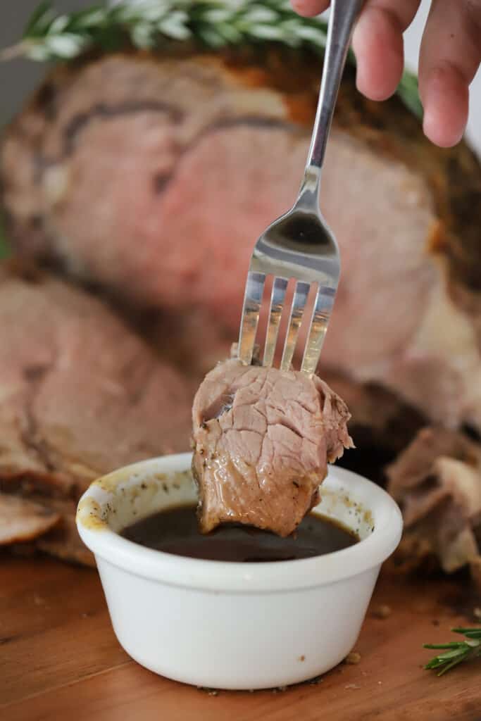 A fork holding a piece of beef being dipped into au jus.