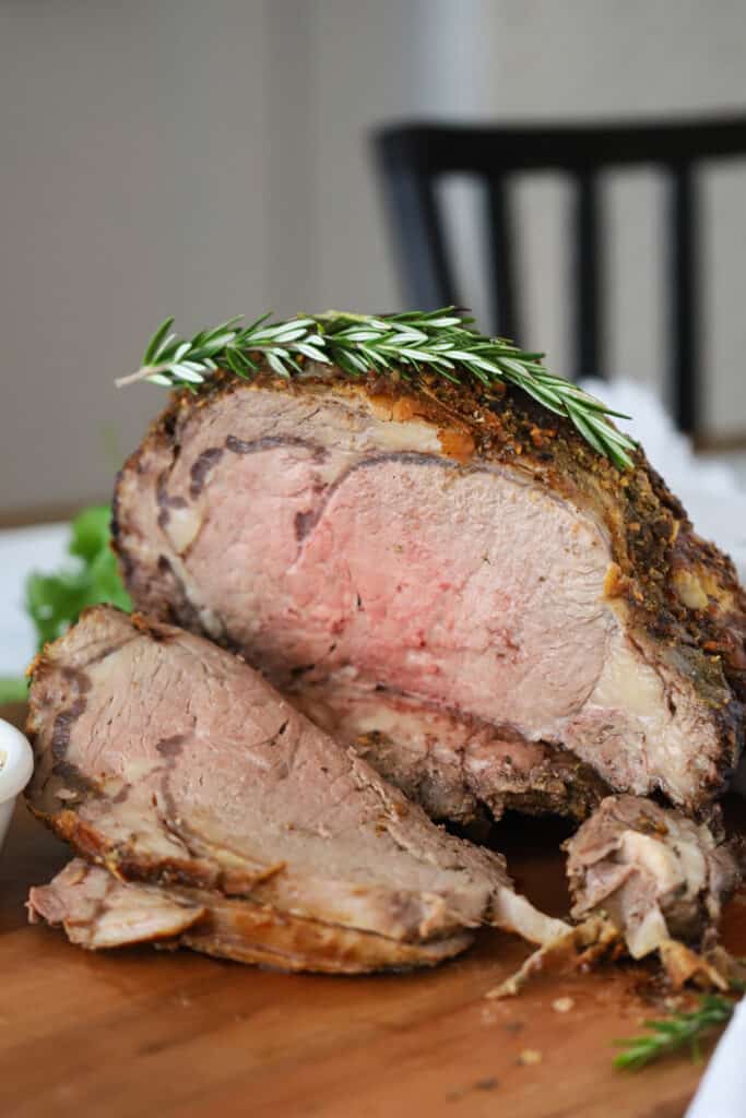 A cutting board with roast beef sliced and garnished with fresh rosemary. prime rib boneless, Prime rib temp, best way to reheat prime rib. 