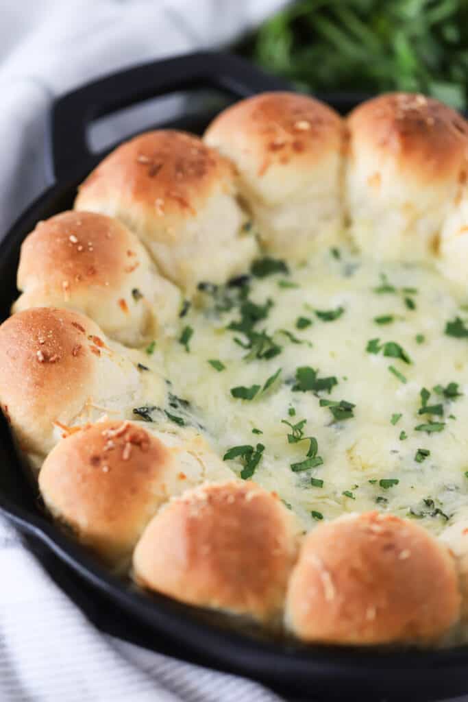 A skillet with a ring of baked dinner rolls and spinach dip in the center.