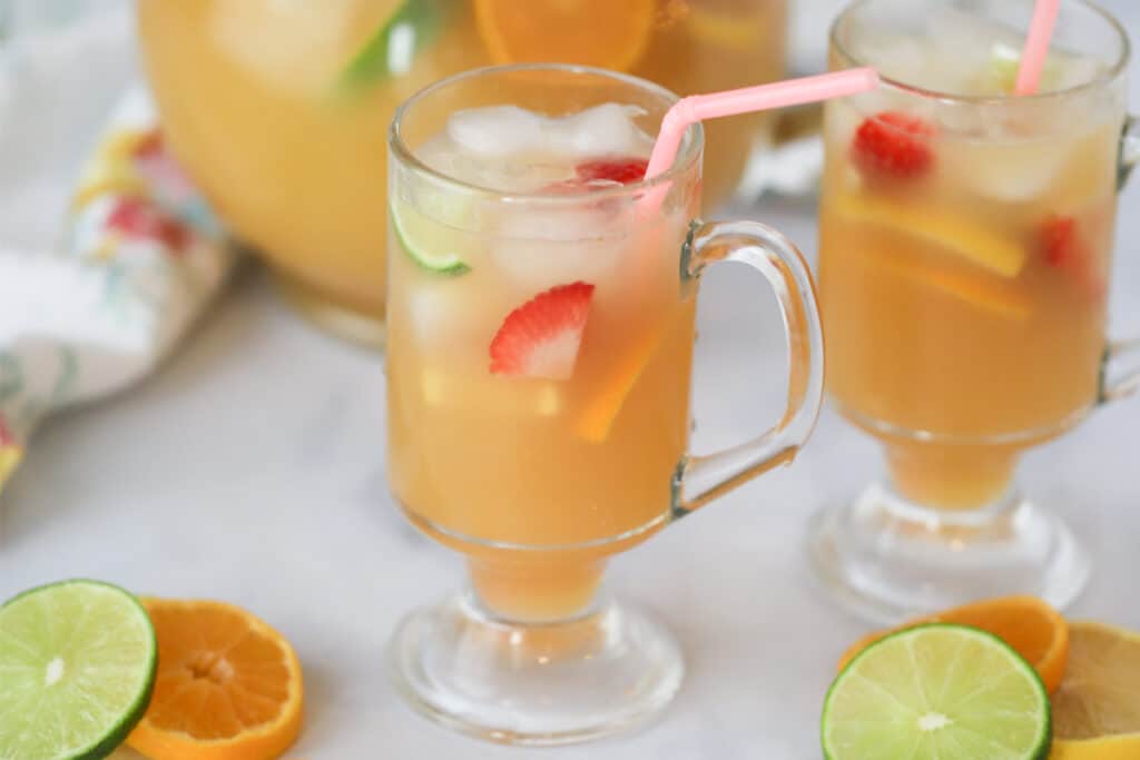 Tropical punch in glass mugs with fresh fruit, ice, and colorful straws.