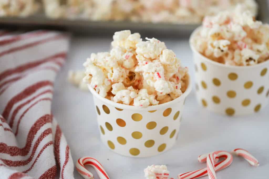 Small decorative cups full of Candy Cane Popcorn on a table. white chocolate peppermint popcorn recipe. 
