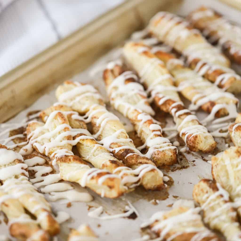 A baking sheet full of cinnamon puff pastry twists drizzled with icing. cinnamon twists recipes, puff pastry twists cinnamon. Cinnamon twists.