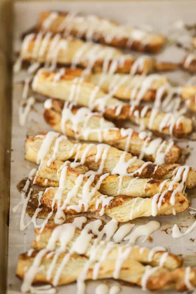 Cinnamon Twists made with puff pastry and drizzled with icing on a baking sheet.