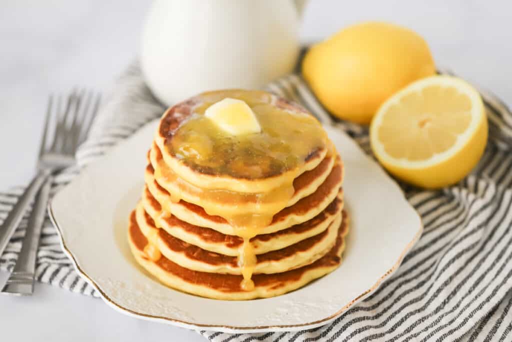 A stack of Lemon Ricotta Pancakes topped with melted butter on a white serving plate. Lemon ricotta pancakes recipe. Easy ricotta pancakes.