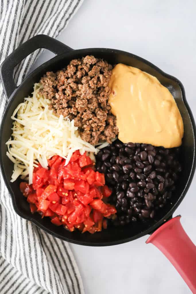 A cast iron skillet full of the ingredients to make this queso dip. baked queso dip with ground beef. Velveeta queso recipe, best cowboy queso.