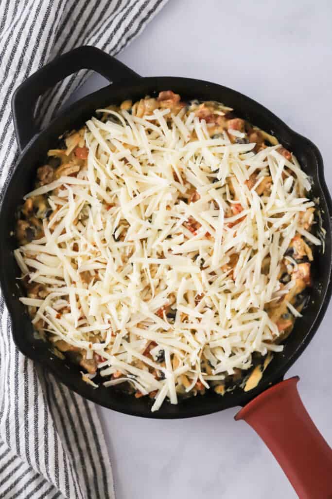 A cast iron skillet with queso topped with shredded cheese; loaded queso dip; cowboy queso, rotel queso.